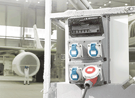 Eine graue AMAXX® Steckdosenkombination hängt in einer Flugzeugbauhalle
