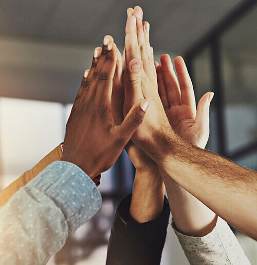 Unternehmenskultur Mehrere Hände unterschiedlicher Personen klatschen im Büro zu einem gemeinsamen High-Five.